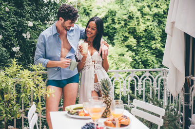 Smiling couple standing against trees in balcony