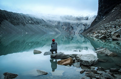 Woman sitting on rock against mountains in lake during winter