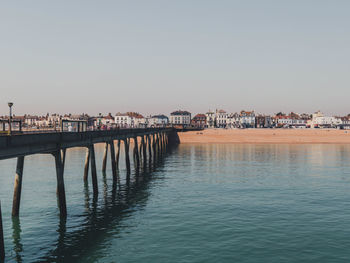 Bridge over sea by buildings against clear sky