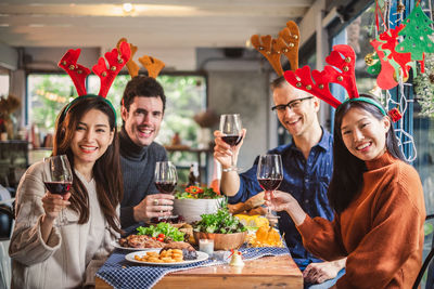 Portrait of happy friends with red wine in restaurant during christmas