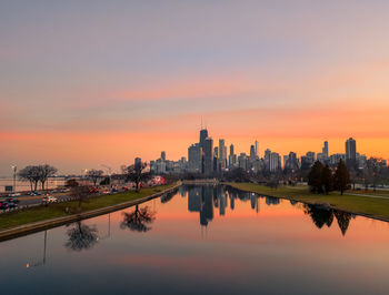 Reflection of buildings in city against sky during sunset