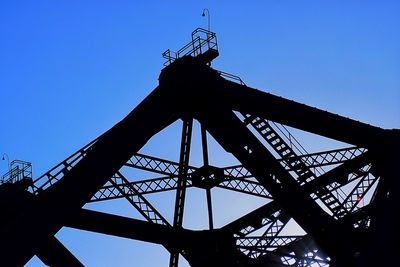 Low angle view of silhouette crane against clear blue sky