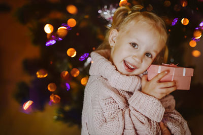 Cheerful baby girl with a gift box on the background of festive christmas tree on new year's eve