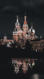 Illuminated building by river against sky in city at night