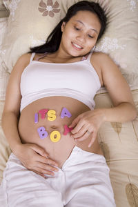 High angle view of pregnant woman with text on stomach lying on bed