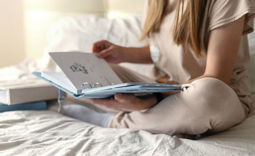Low section of woman reading diary sitting on bed at home