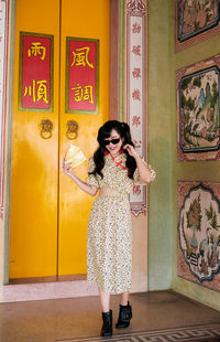 Portrait of woman in yellow modern cheongsam holding a red envelope at chinese temple 