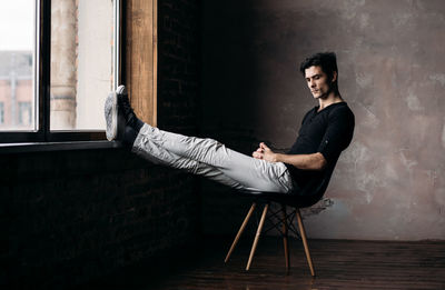 Young man relaxing on chair by wall