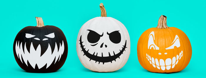 Three spooky halloween pumpkins with scary face expressions over pastel blue background. 