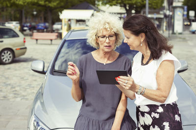 Senior female friends using digital tablet against car on street