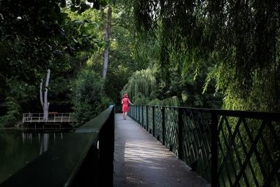 Rear view of woman walking on metallic footbridge over pond at park