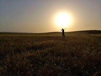 Silhouette man walking with gun walking on field at sunset