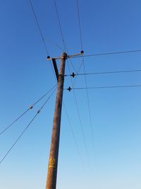 Low angle view of electricity pylon against clear blue sky