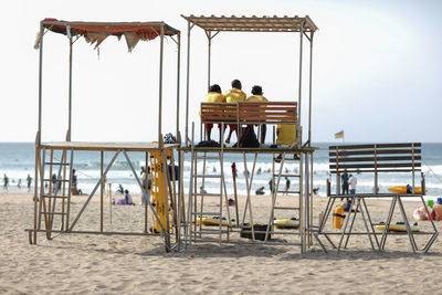 Rear view of men sitting at lifeguard hut against sky