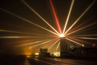 Light beams emitting from lighthouse by sea at night