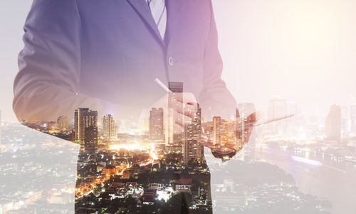 Double exposure of businessman standing against modern illuminated buildings in city