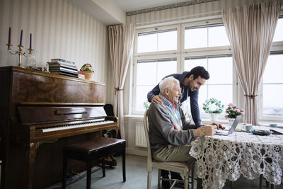Happy man using laptop with caretaker in nursing home