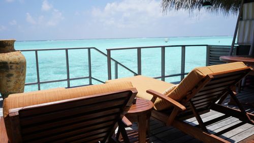 Empty chairs and table by sea against sky