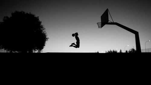 Silhouette man playing with basketball against sky