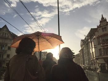 People walking in city against cloudy sky