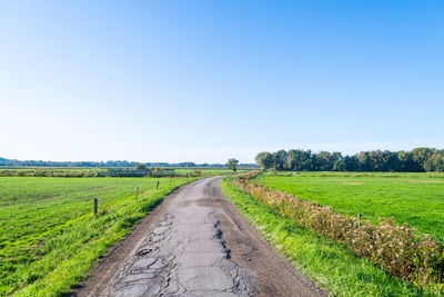 Road passing through agricultural field against clear sky