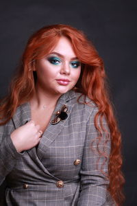 Portrait of sensuous young woman wearing gray blazer while sitting against black background