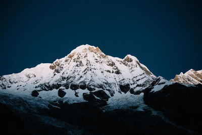 Low angle view of snowcapped mountains against clear blue sky