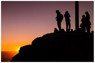 Silhouette people on cliff against clear sky during sunset