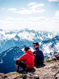 People sitting on snow covered mountain against sky