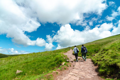 Rear view of men walking on footpath against sky