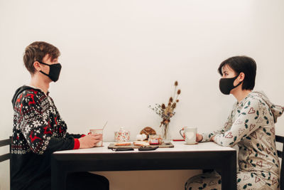 Side view of young man and woman wearing mask sitting at cafe