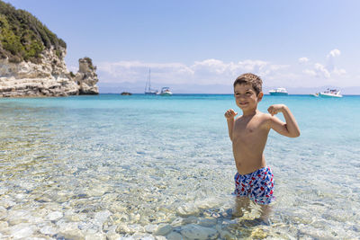 Portrait of shirtless man standing on beach against sky