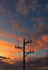 Low angle view of silhouette electricity pylon against dramatic sky