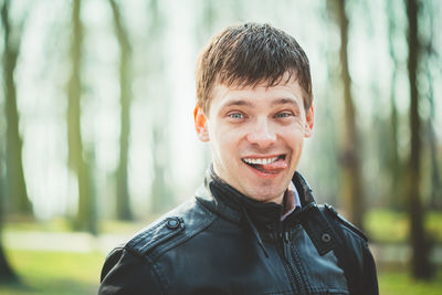 Portrait of smiling man sticking out tongue against trees