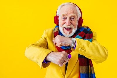 Senior man dancing while listening music against yellow background