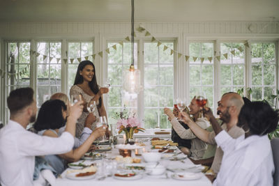 Smiling woman toasting drink with family members during dinner party at home