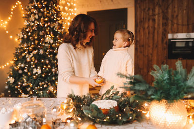 Happy mom and daughter in sweaters together prepare a festive cake for the christmas holiday at home