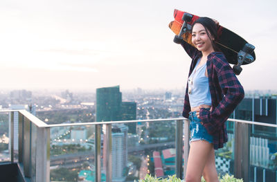 Portrait of smiling young woman standing against railing in city