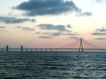 Suspension bridge over sea against sky during sunset