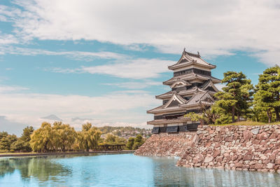 Traditional building by lake against sky