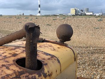 Close-up of rusty metal structure on field against sky