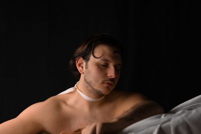 Portrait of shirtless young man lying on bed