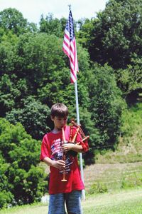 Boy holding umbrella standing against trees