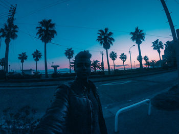 Portrait of young man standing by palm trees against sky