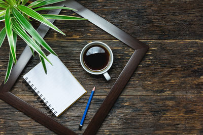 High angle view of coffee with plant by note pad and pencil on wooden table