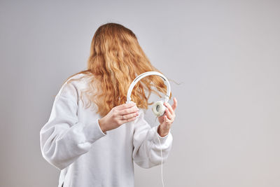 Young woman holding headphones while standing against gray background
