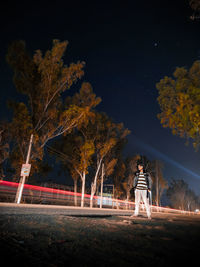 Low angle view of a mysterious pedestrian man walking on road with light trails at night 