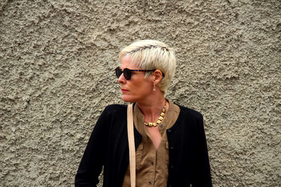 Mature woman wearing sunglasses against wall