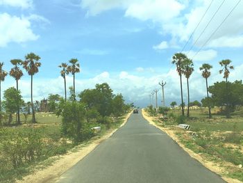 Road amidst trees on field against sky