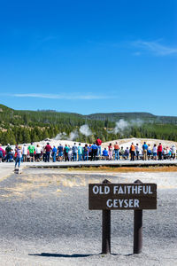 People looking at geyser against blue sky